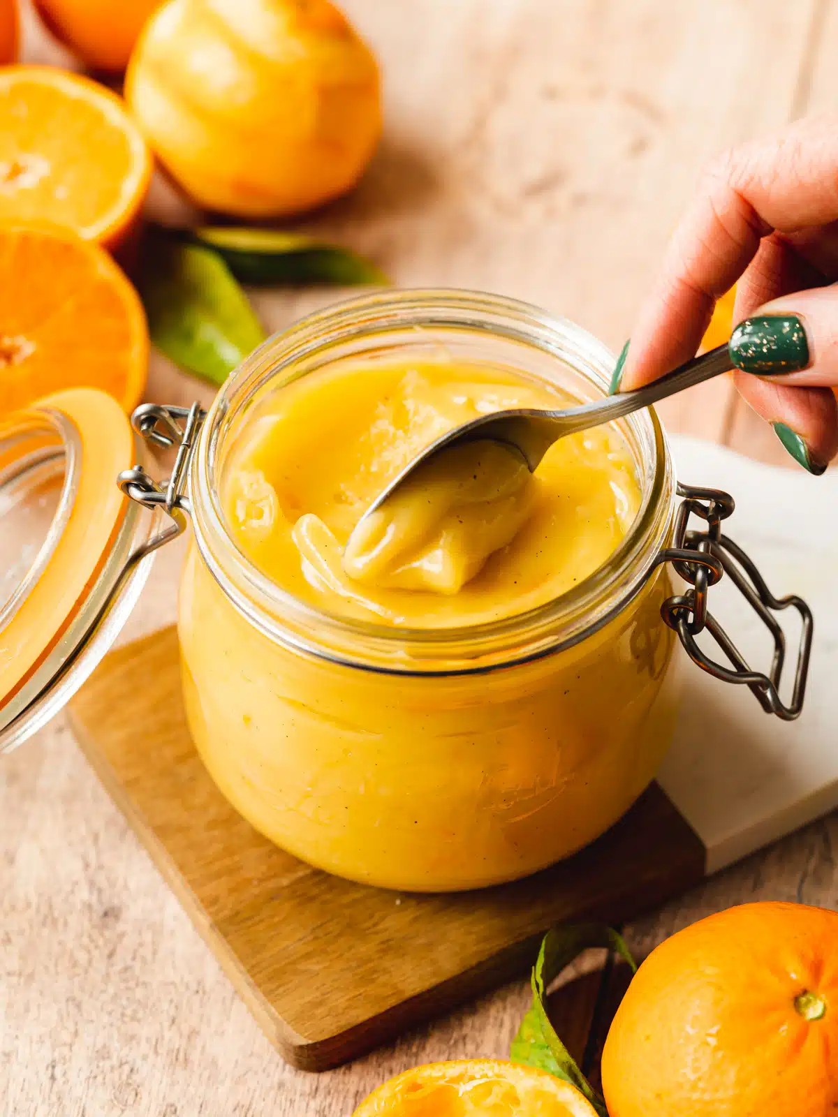 orange curd in a jar being scooped out with a spoon.