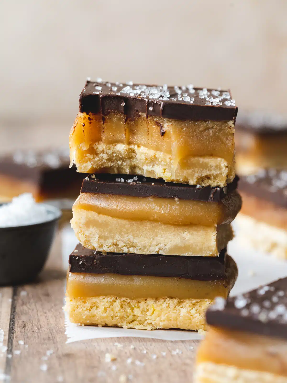 a stack of millionaire shortbread bars on a piece of parchment paper with sea salt sprinkled on top of them.