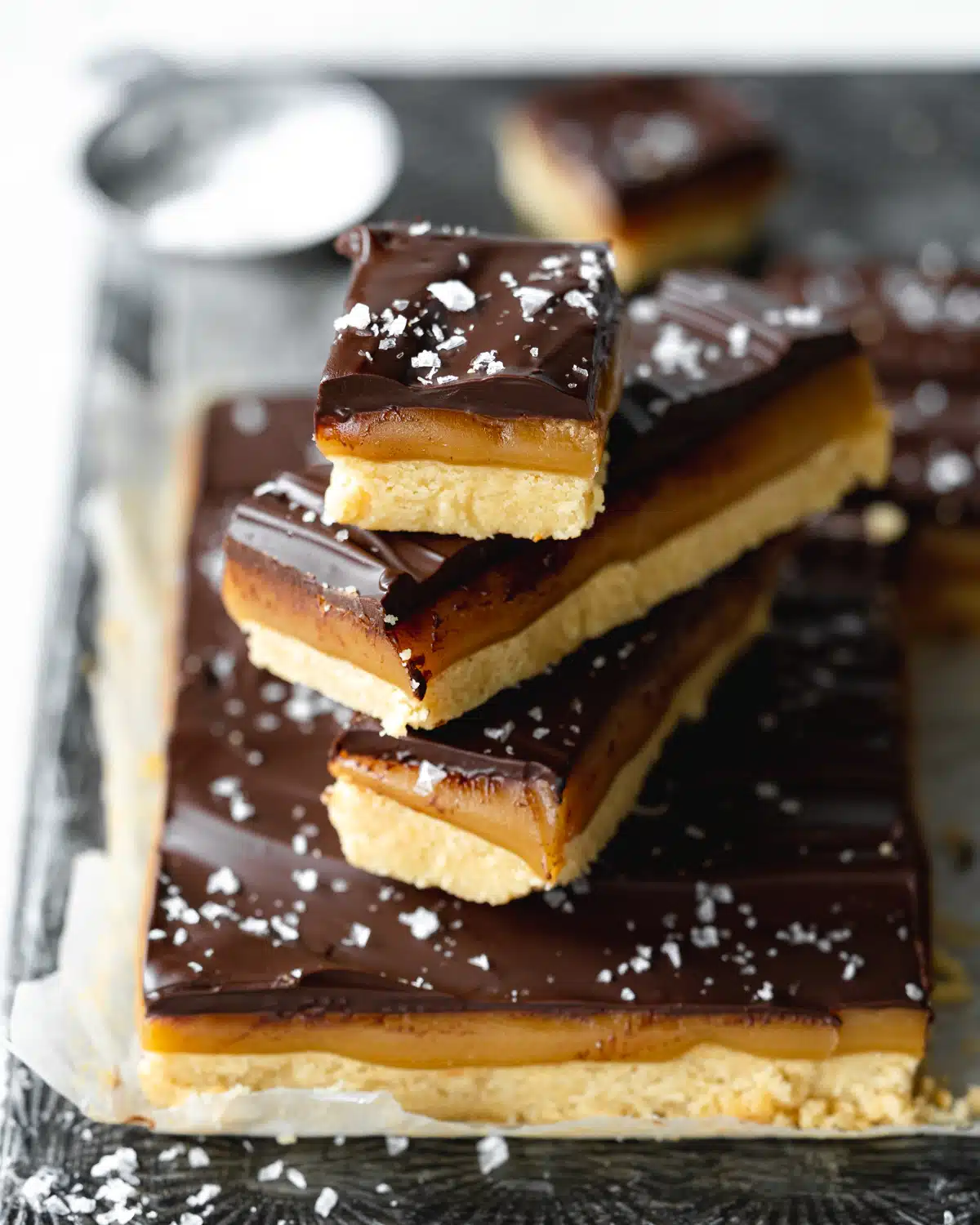 stack of caramel slices on a metal tray with sea salt on top.