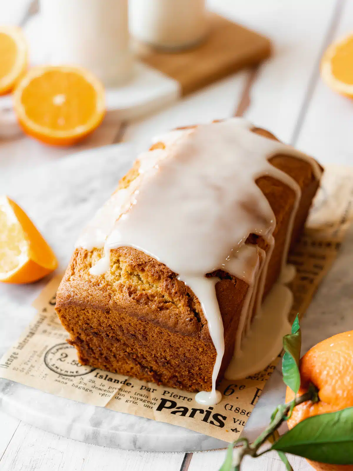 an orange loaf cake with icing drizzled on top of a marble slab.