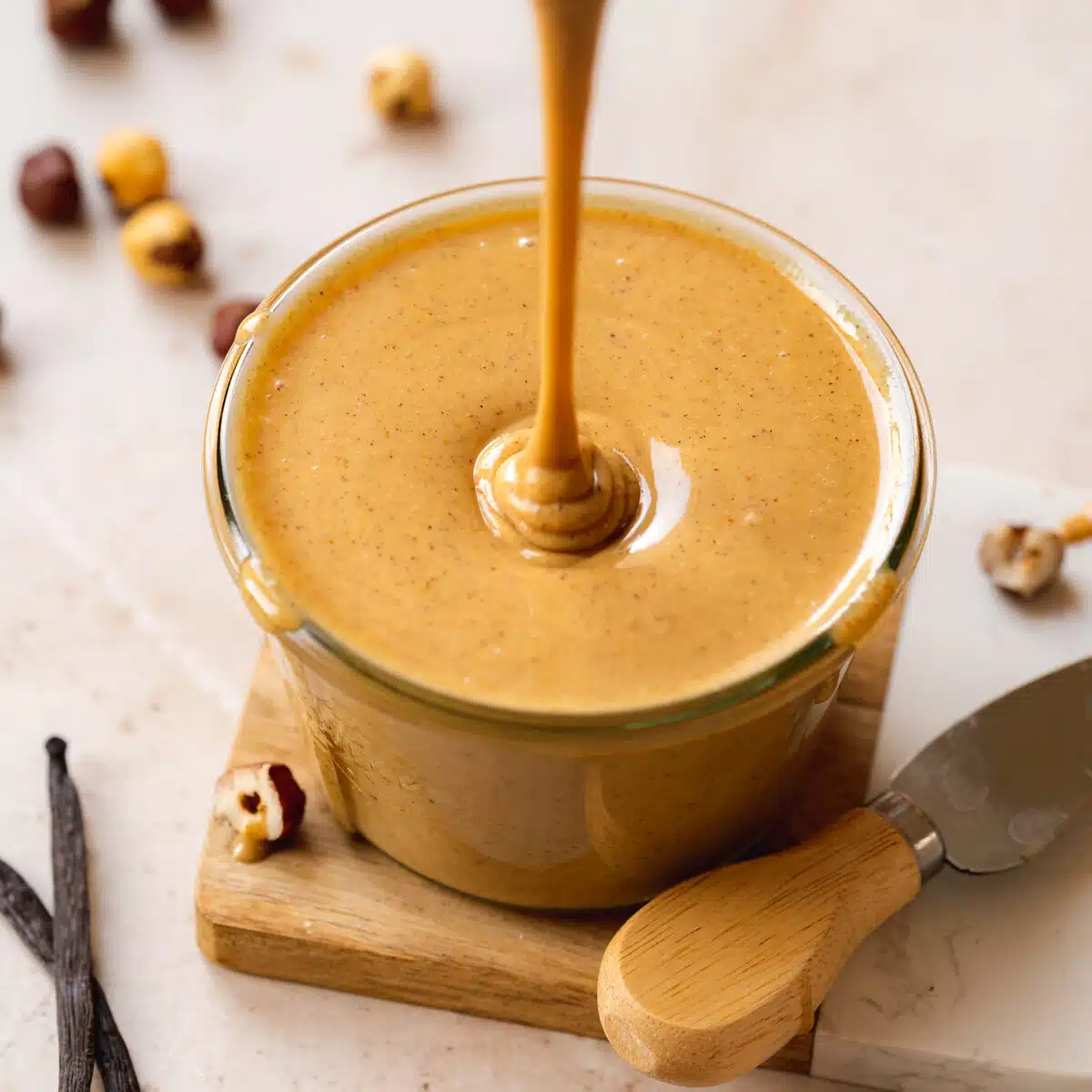 hazelnut butter dripping into a jar with roasted hazelnuts scattered around it.