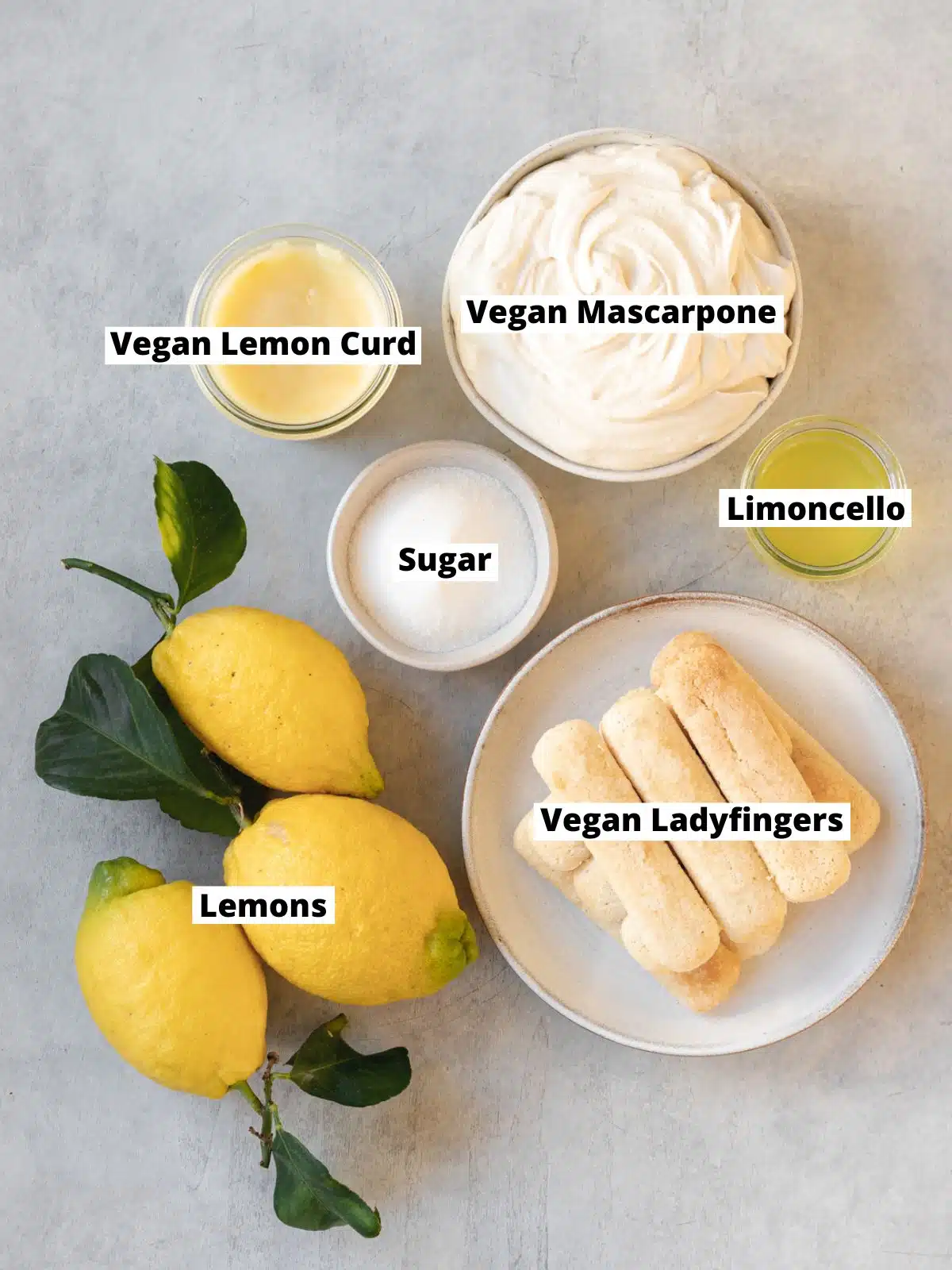 ingredients for vegan limoncello tiramisu measured out in bowls on a grey surface.
