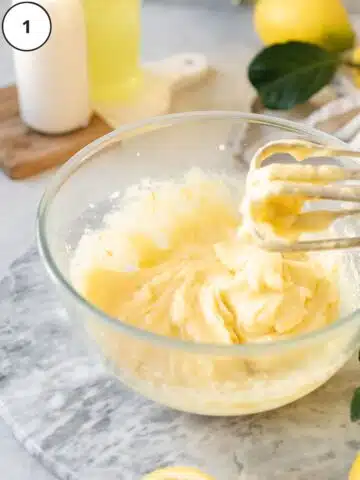 lemon mascarpone whisked in a bowl with an electric whisk on top and lemons in the background.