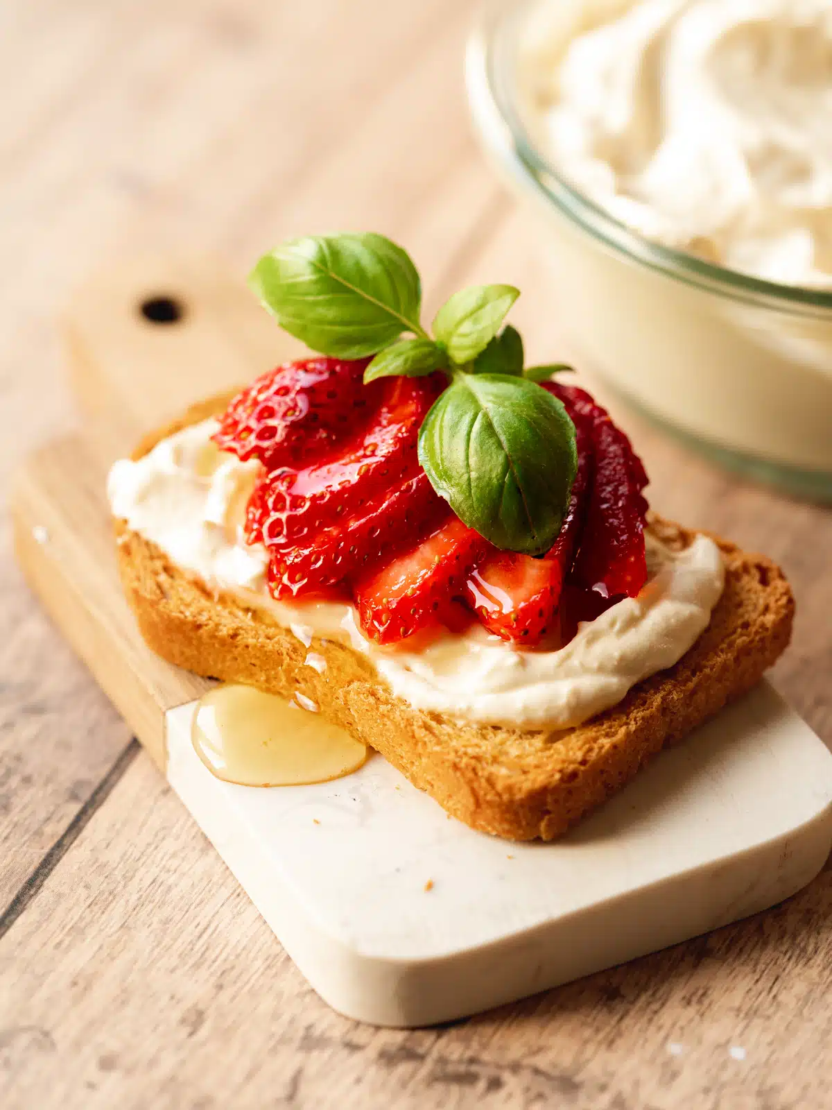 a slice of toast with fresh mascarpone, strawberries, syrup and fresh basil on top.