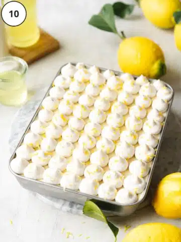 tiramisu with piped cream topping and lemon zest in a rectangular baking dish with fresh lemons around it.