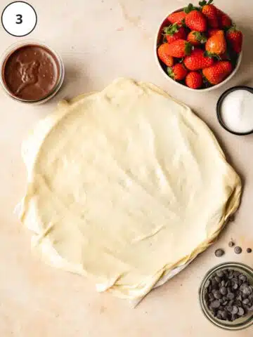rolled out pizza dough on a pizza tray with nutella and strawberries around it.