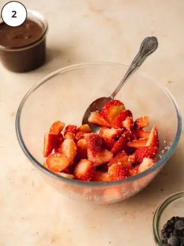 strawberries macerating with sugar in a bowl with a spoon in it.