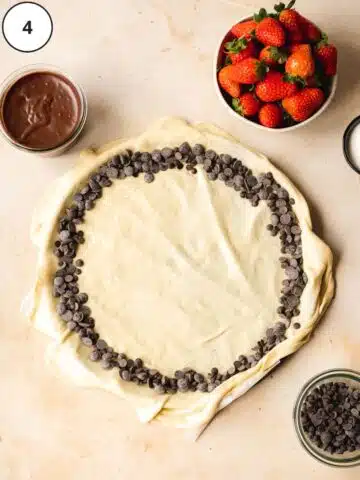 pizza on a tray with a chocolate rim and a bowl of strawberries next to it.