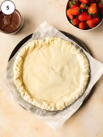 rolled out pizza dough with a chocolate stuffed crust and a bowl of strawberries next to it.