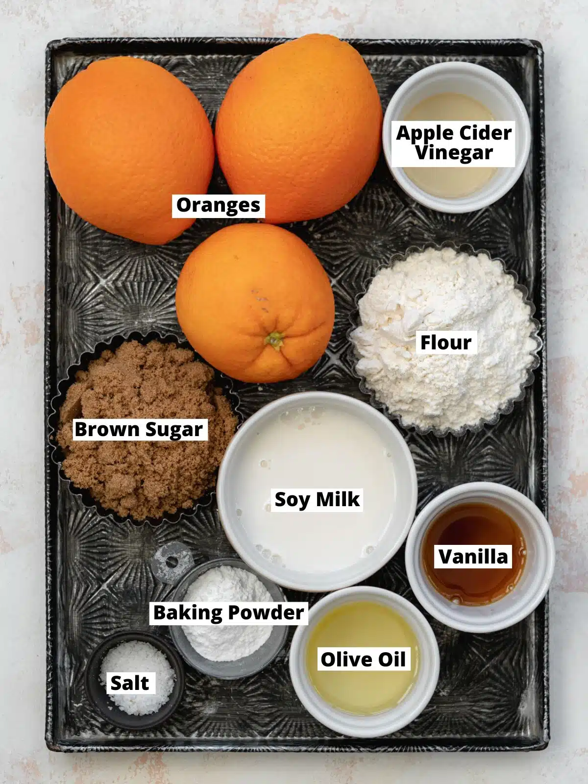 ingredients for orange cake measured out in bowls on a vintage metal tray.