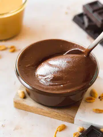 45 degree angle shot of a small glass bowl of chocolate peanut butter with a spoon in it.