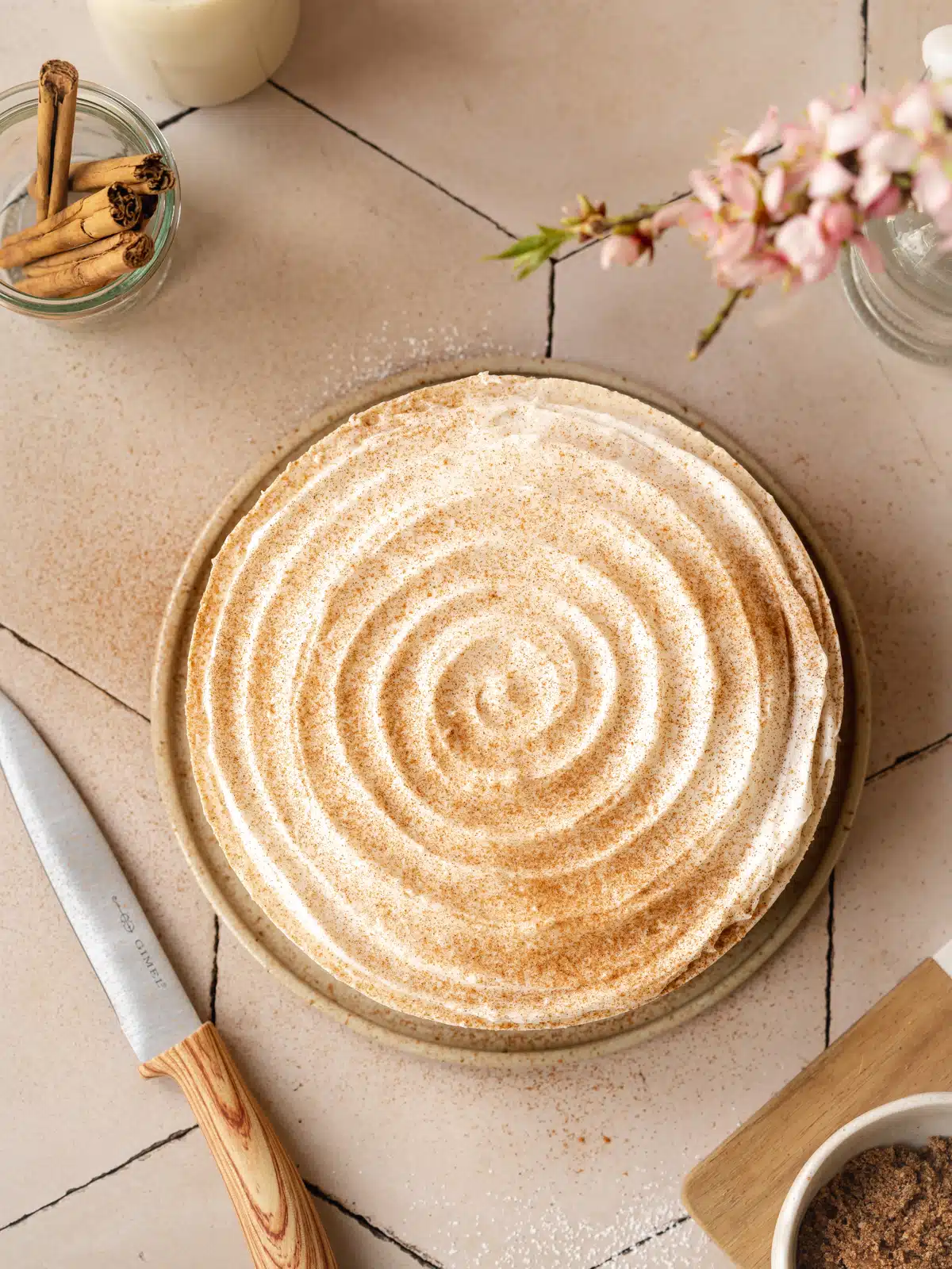Overhead shot of vegan cinnamon roll cheesecake in the pan with a pretty swirl design and light dusting of cinnamon sugar over the top.
