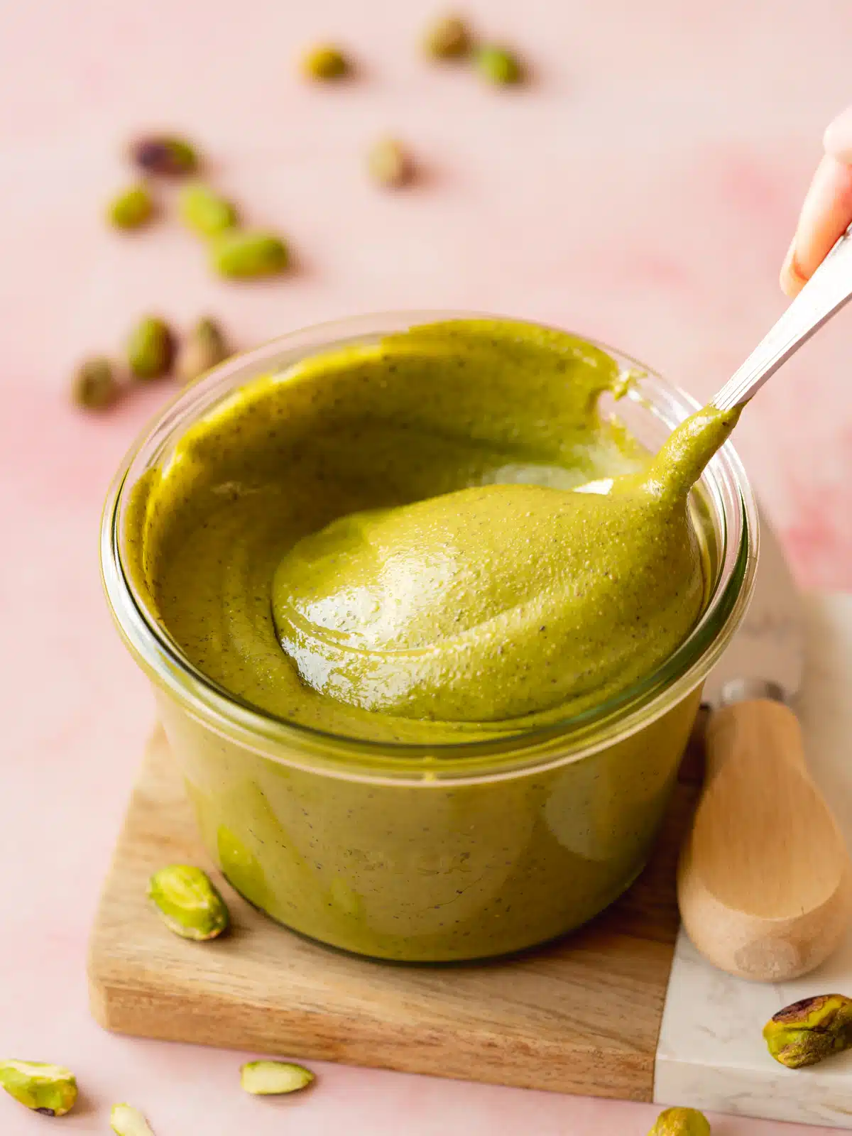 a spoon stirring a glass jar of pistachio butter showing the thick texture.
