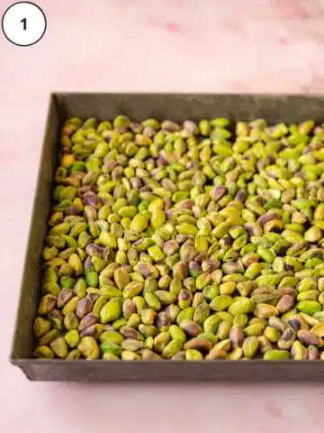 vibrant green raw pistachios laid out on a baking sheet with a pink marble background.
