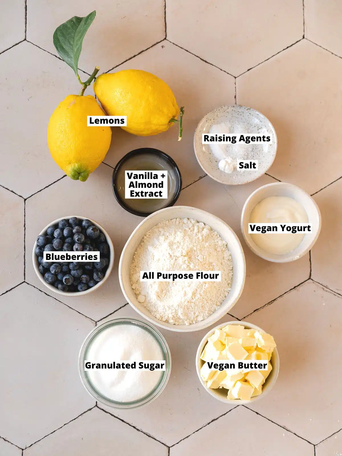 overhead shot of individual ingredients needed to make lemon blueberry cookies measured out into bowls on a white hexagonal background with text overlay.