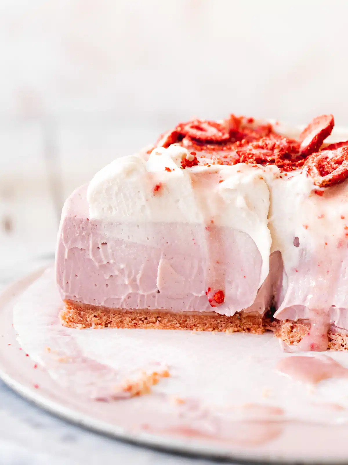 strawberry cheesecake with whipped dairy-free cream and freeze dried berries on top, with slices taken out of it showing the creamy consistency.