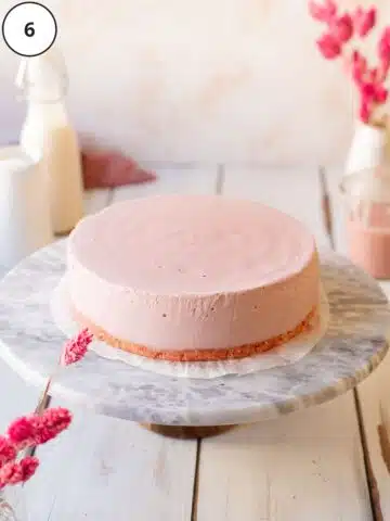 vegan strawberry cheesecake on a marble turntable with pink flowers and a jug of milk in the background.