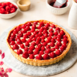 vegan french raspberry tart filled with dairy-free pastry cream and topped with raspberries on a marble surface.