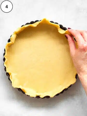 a hand pressing sweet pastry into a tart tin.