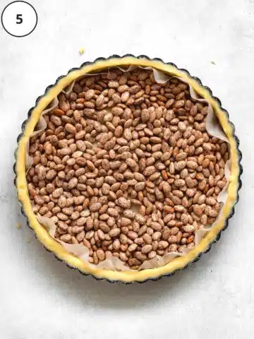 a raw tart crust in a tin with parchment and baking beads on top.