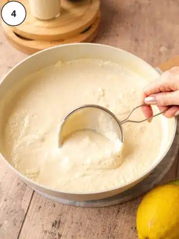 ricotta cheese curds being scooped out of a large saucepan using a small fine-mesh sieve.