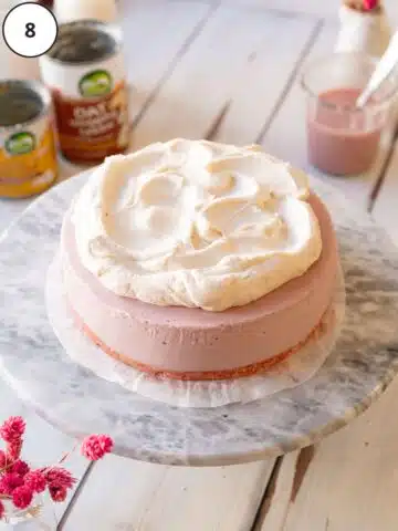 pink vegan cheesecake with whipped cream topping on a marble surface.