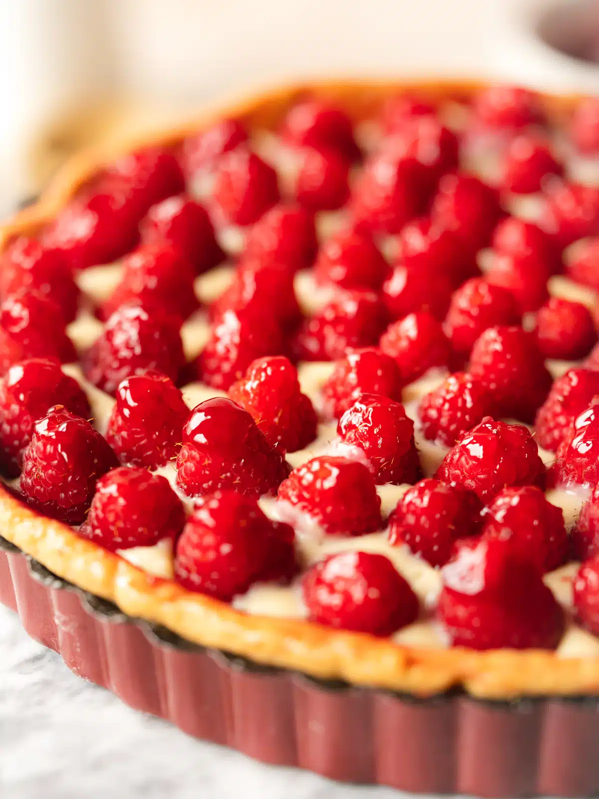 close up of raspberry tart showing the glossy berries glazed with raspberry jam on a layer of dairy-free custard.