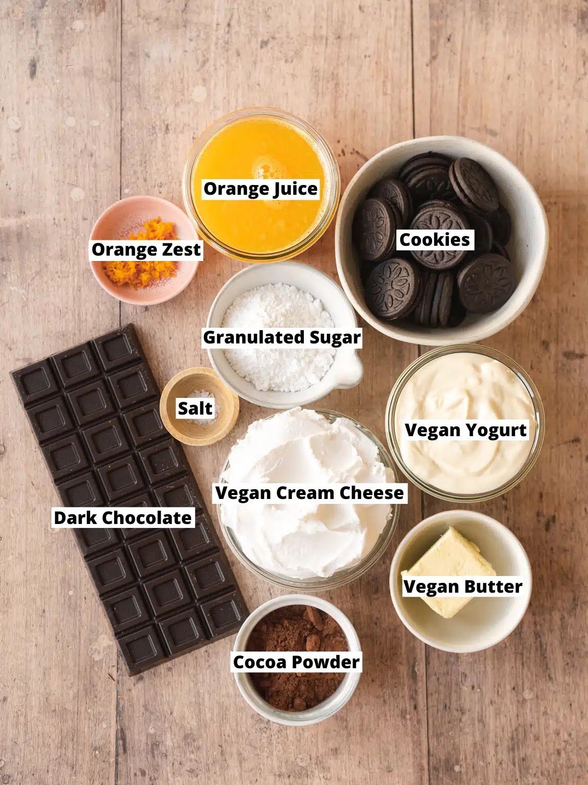 Ingredients needed to make vegan chocolate orange no bake cheesecake measured out into bowls on a wooden table.