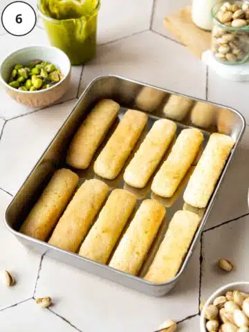 a rectangular baking pan with a layer of vegan ladyfingers laid out in it.