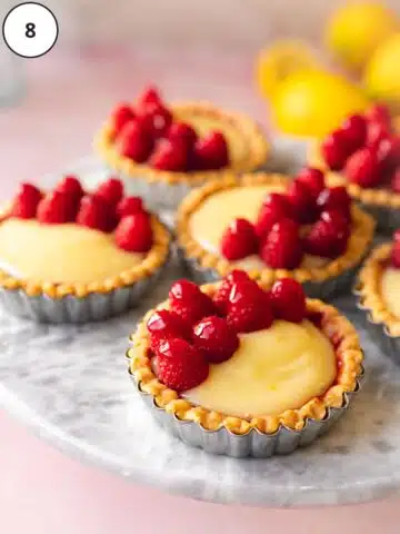 Vegan mini lemon curd tarts are topped with raspberries that have been glazed with raspberry jam for serving.