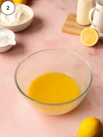 a bowl with melted butter, lemon and sugar with fresh lemons scattered around it on a pink surface.