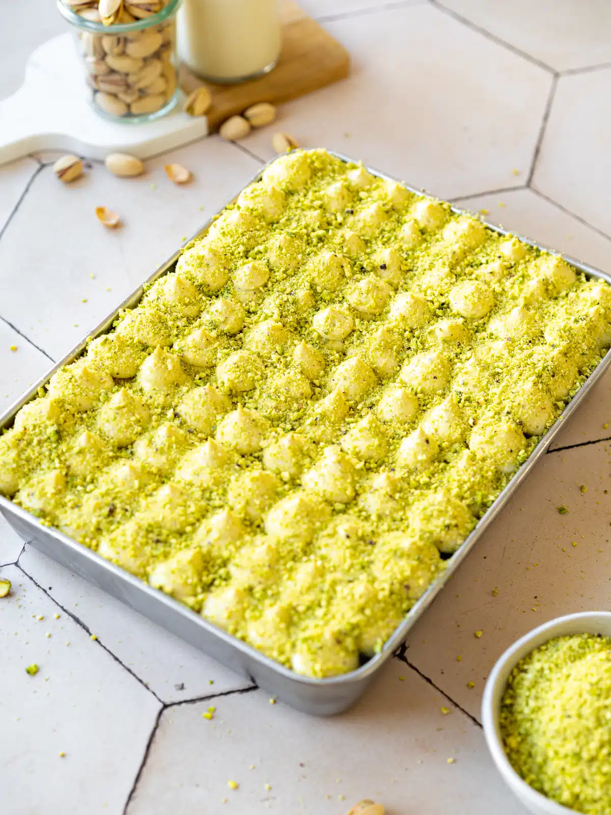 a pistachio tiramisu in a rectangular pan with bright green ground pistachios on top.