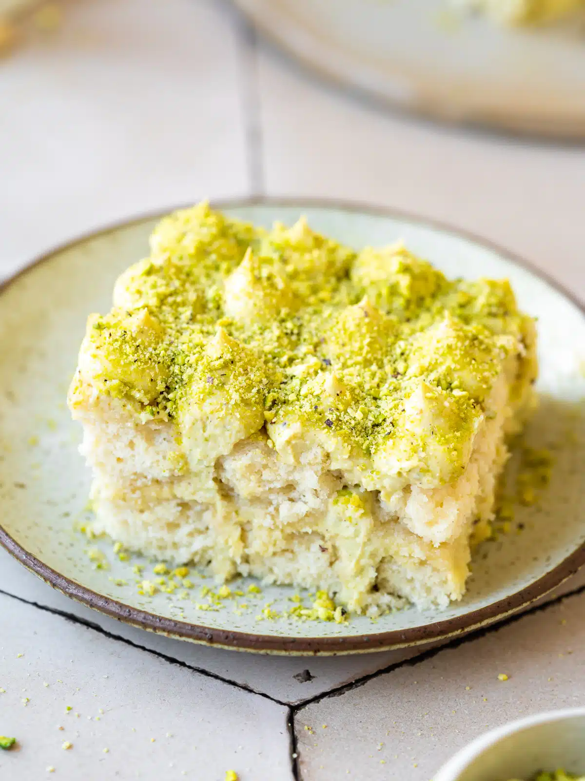 a slice of pistachio tiramisu on a ceramic plate with bright green pistachio pieces on top.