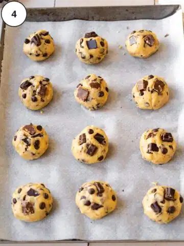12 balls of vegan chocolate chip cookie dough on a parchment lined baking sheet to chill before baking.