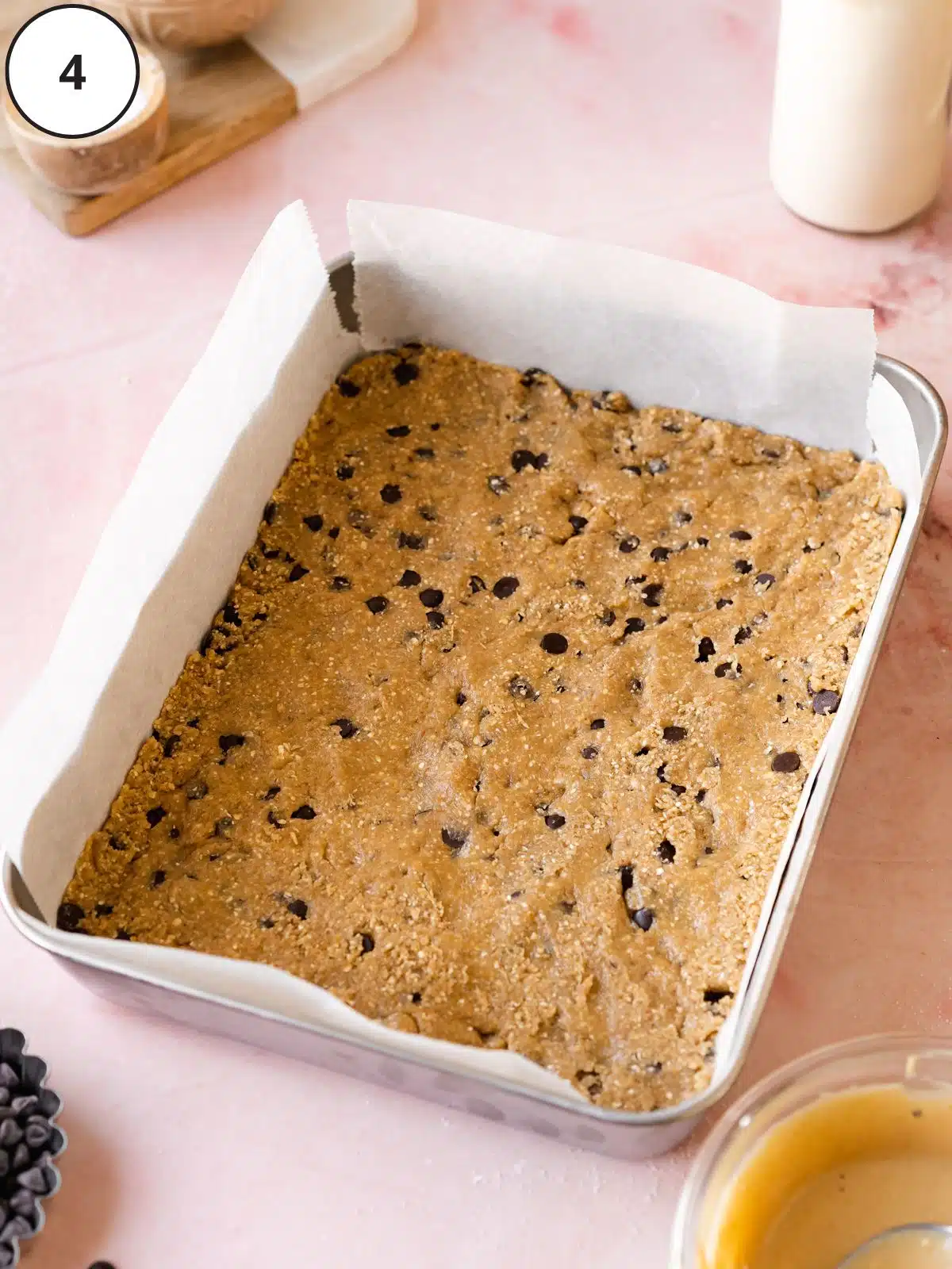 Parchment-lined baking tin with a layer of edible cookie dough pressed into the base.