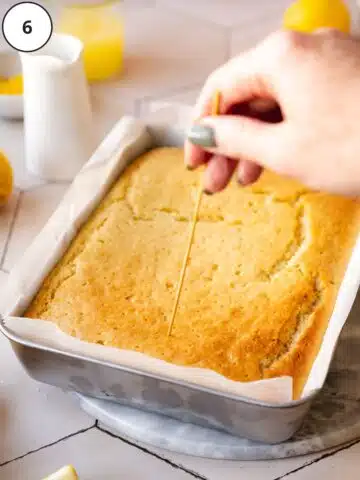 lemon sheet cake with a hand poking holes into it using a bamboo skewer.