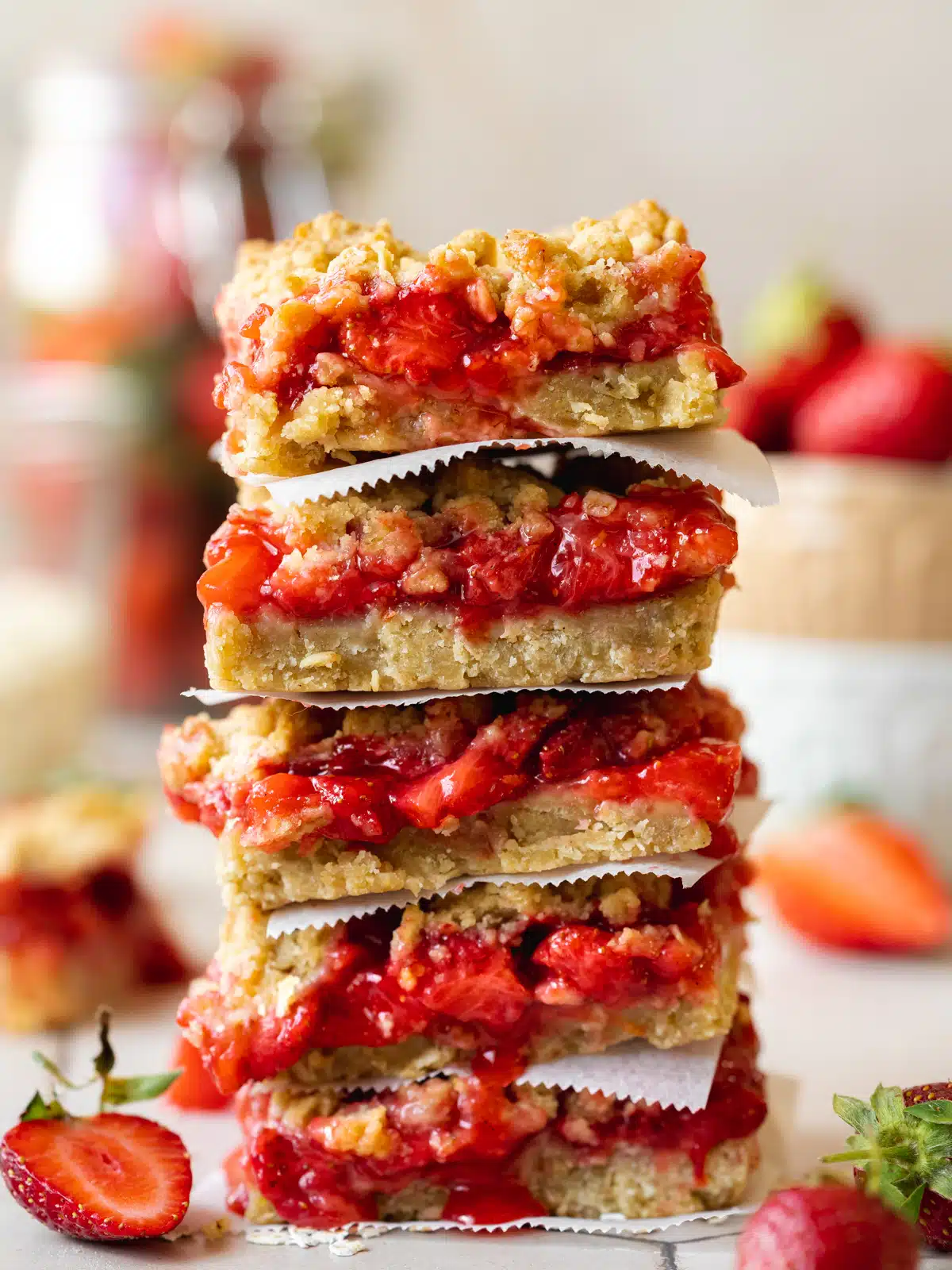 Side-on shot of a vertical stack of oatmeal strawberry crumble bars separated by small pieces of parchment paper.