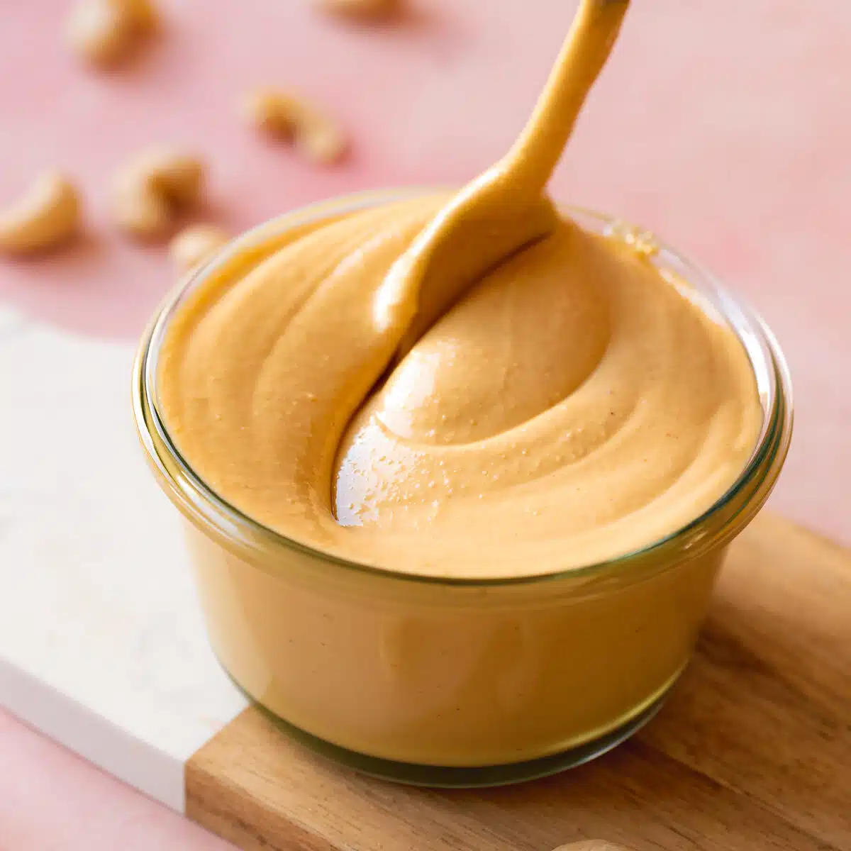 creamy homemade cashew nut butter in a glass jar being swirled with a spoon to show the thick consistency.