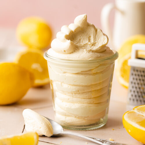 vegan lemon frosting piped into a jar with a spoonfull taken from it showing the creamy consistency.