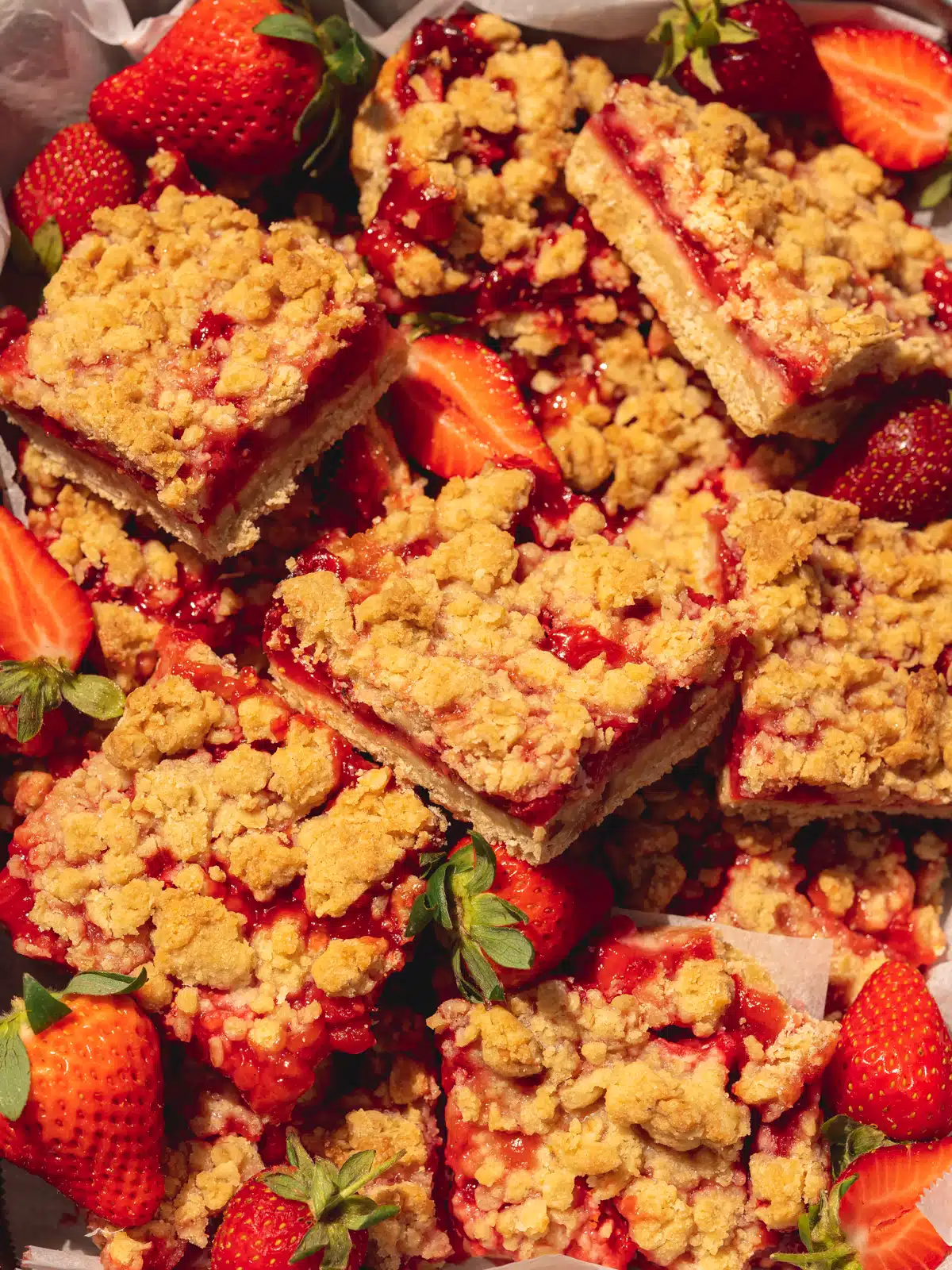 Overhead shot of vegan strawberry crumble oat bars in a pile with fresh strawberries scattered about.