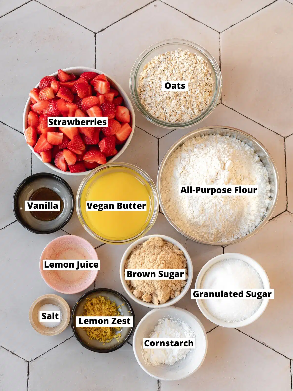 ingredients needed to make vegan strawberry crumble crunch bars measured out into bowls on a white table with text overlay.