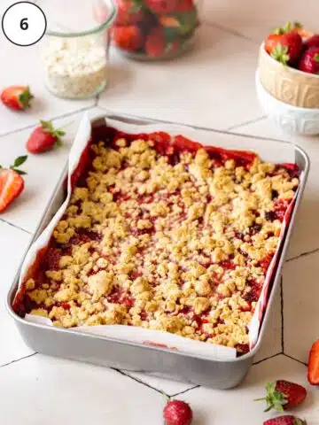 Baked vegan strawberry crumble bars in the baking tin after coming out of the oven. The berry mixture has bubbled up the sides and the crumble topping is golden.