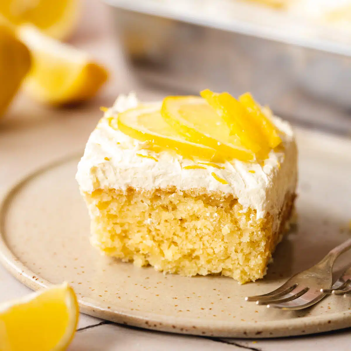 a slice of easy lemon sheet cake on a ceramic plate with a fork and fresh lemon slices on top.