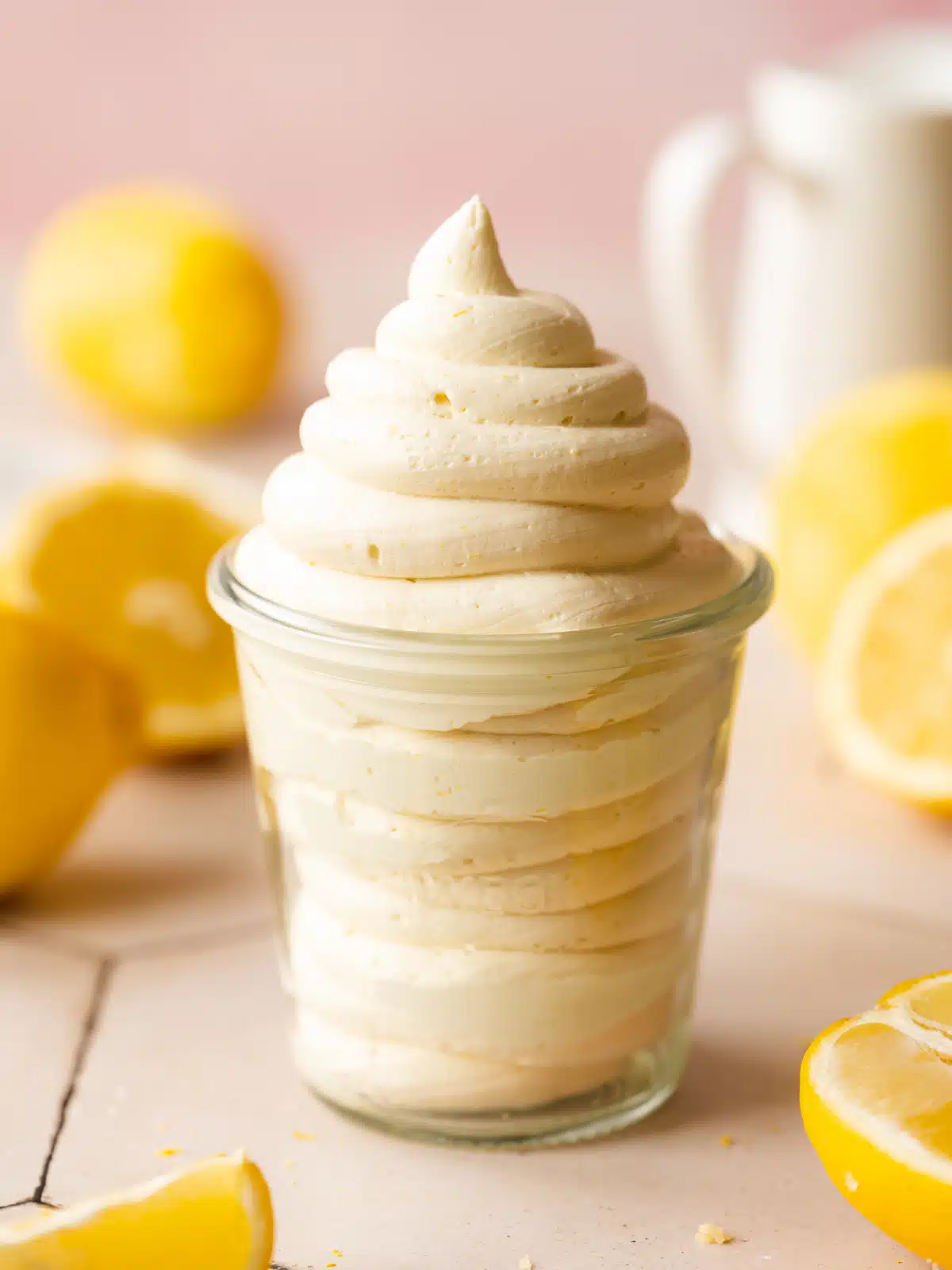 dairy free lemon frosting piped into a glass jar with sliced lemons in the background.