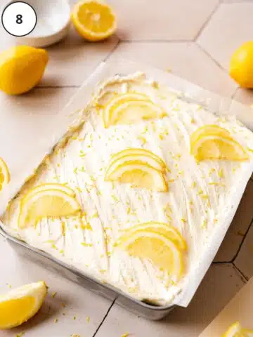 vegan lemon sheet cake with fresh lemon slices on top and fresh lemons scattered around the scene.
