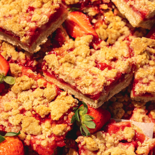 closeup hero shot of vegan strawberry crumble bars in a jumbled pile in the sunshine with fresh berries scattered about.