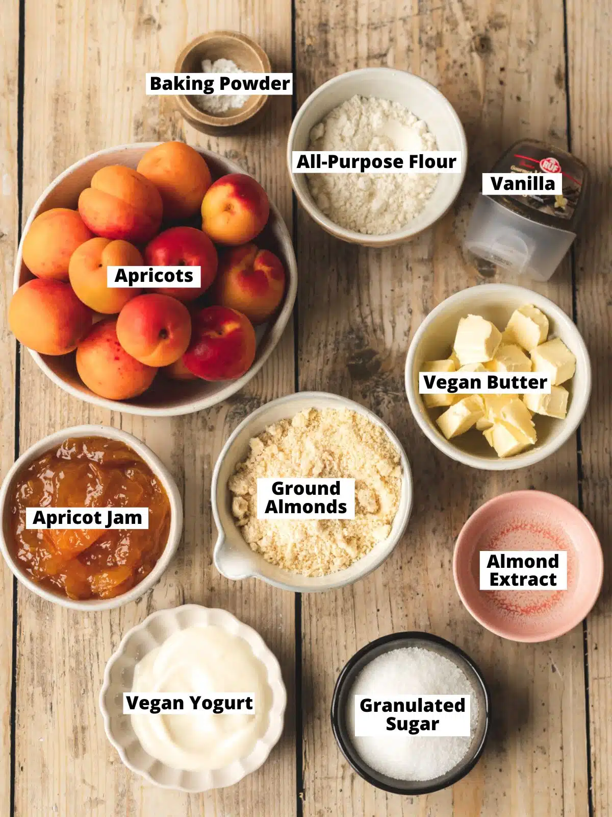 Ingredients needed to make a plant-based almond apricot tart measured out into bowls on a wooden table.