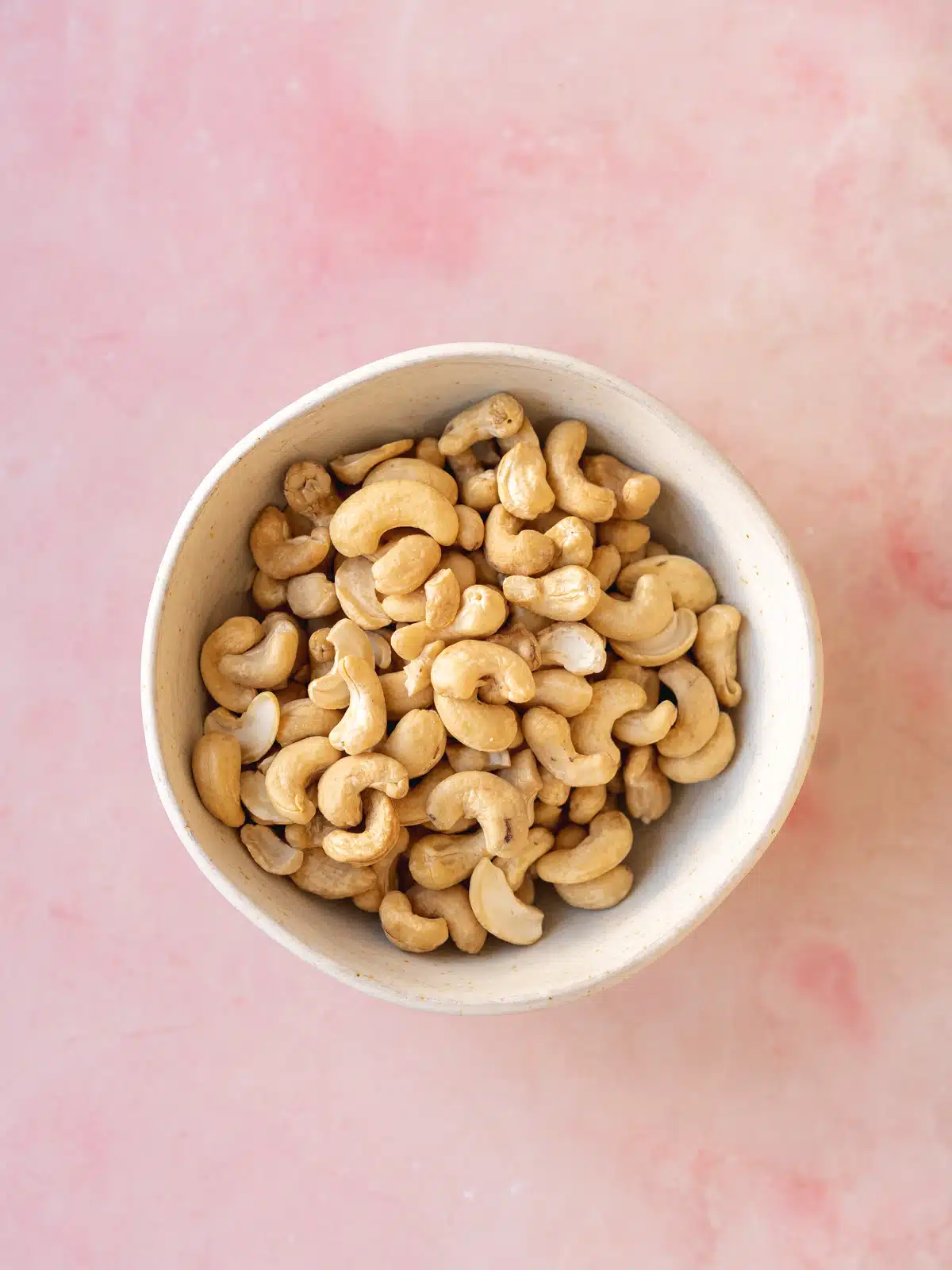 a bowl of raw unsalted cashew nuts on a pink marble surface.