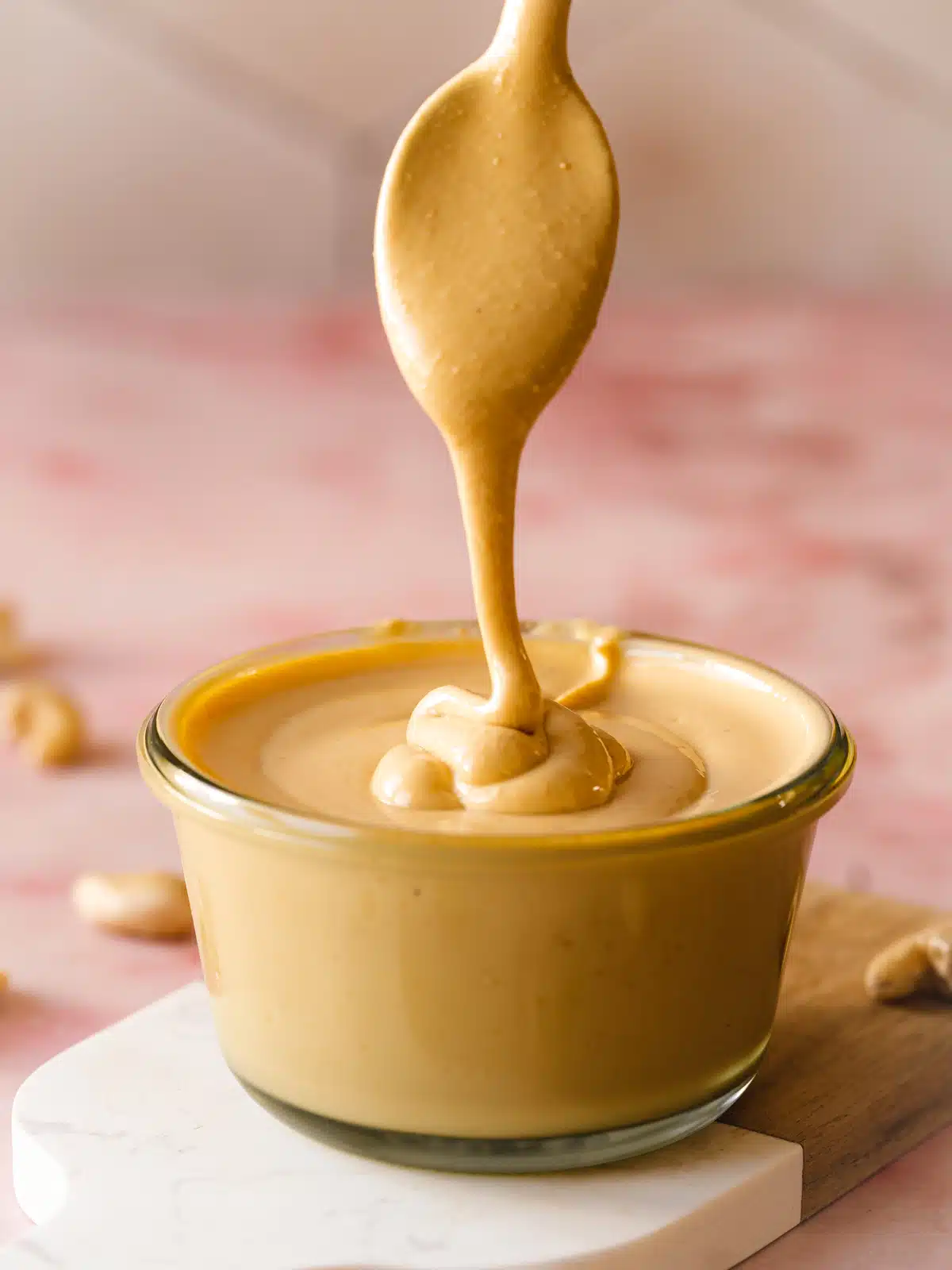 a glass jar with cashew butter being drizzled into it with a spoon showing the creamy texture.