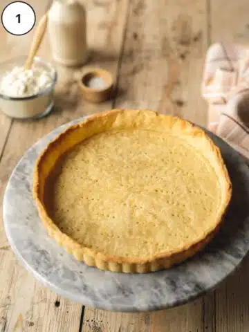 Parbaked vegan tart crust with small fork pricks cooling on a cutting board.